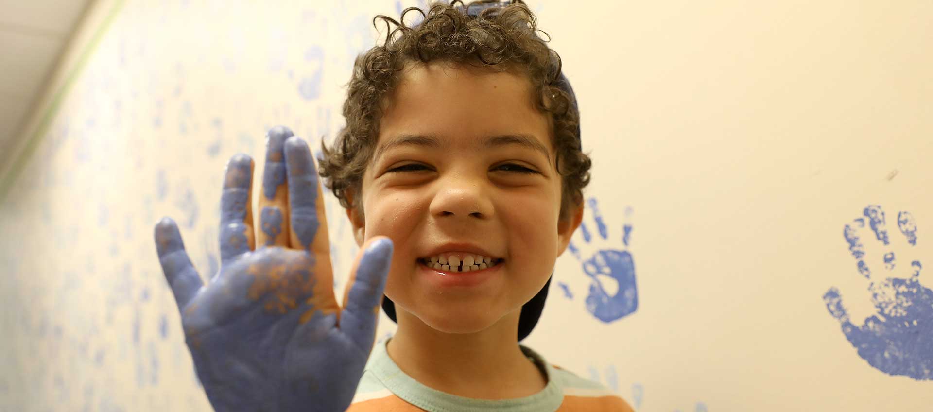 A young students makes a handprint on the community wall