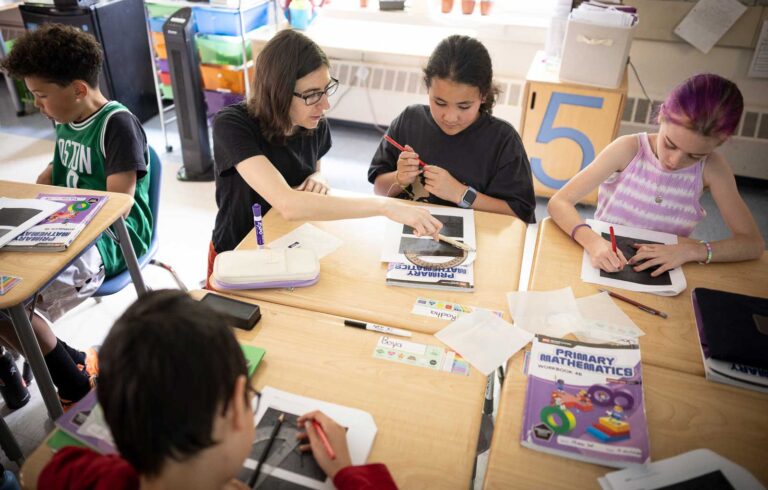 Four students at desks in a circle working with their Primary Mathematics workbooks