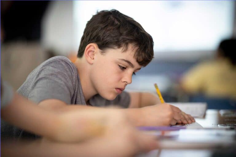 A student holding a pencil leans forward at his desk during a writing assignment
