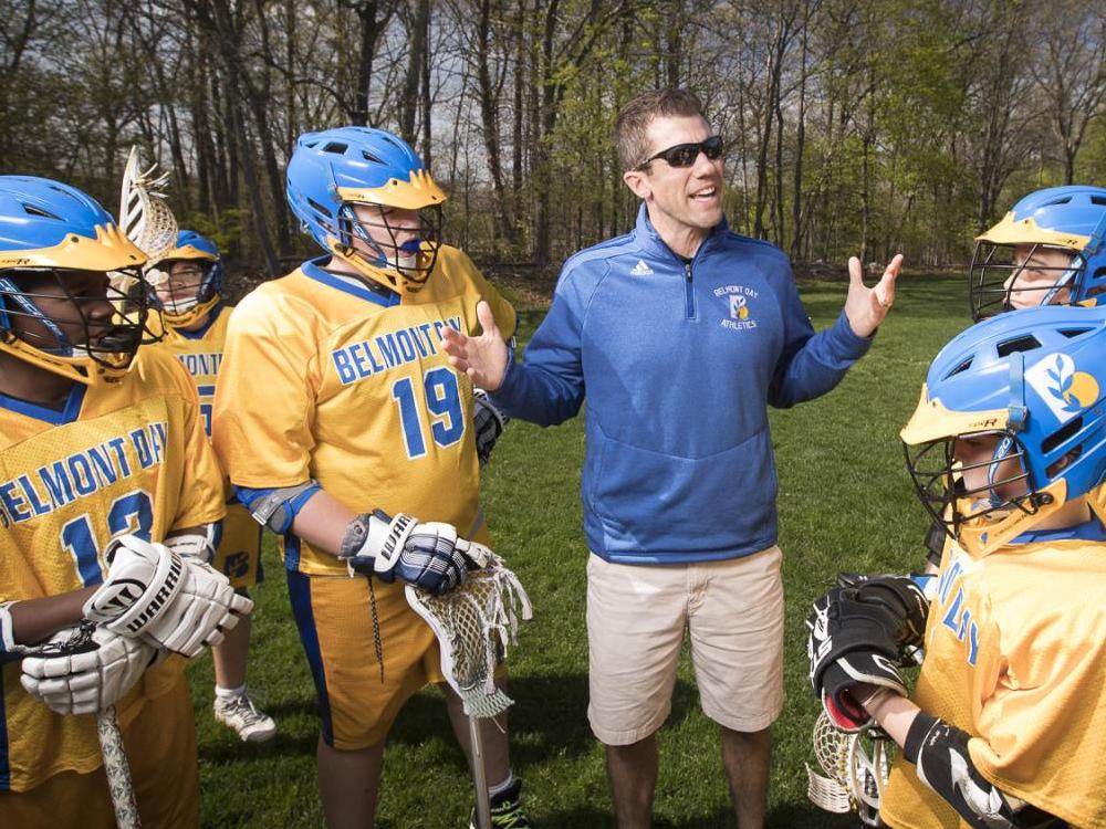 Lacrosse players listen to their coach as the stand around him
