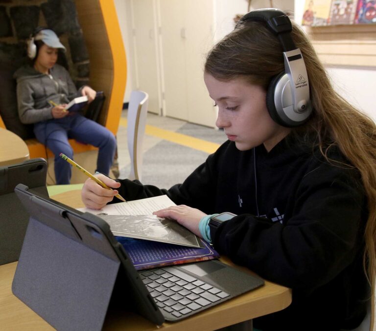Two students sitting in the Erskine Library wearing headphones and working