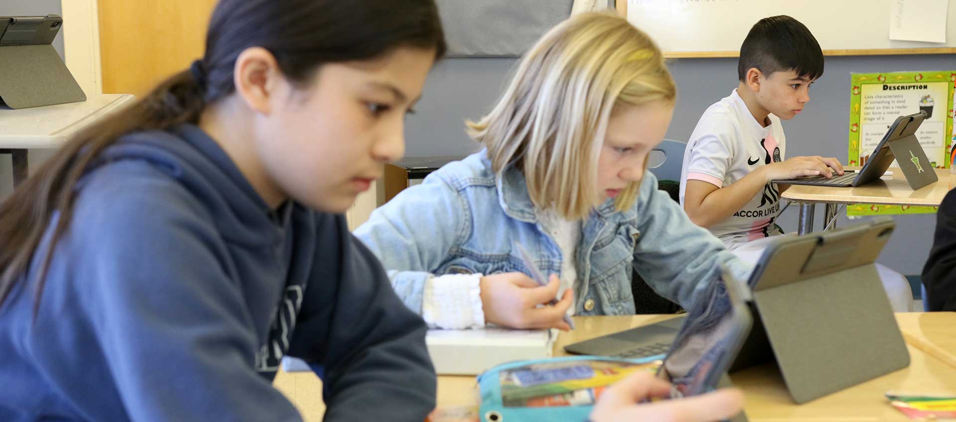 Three seated students with paper notes work on iPads