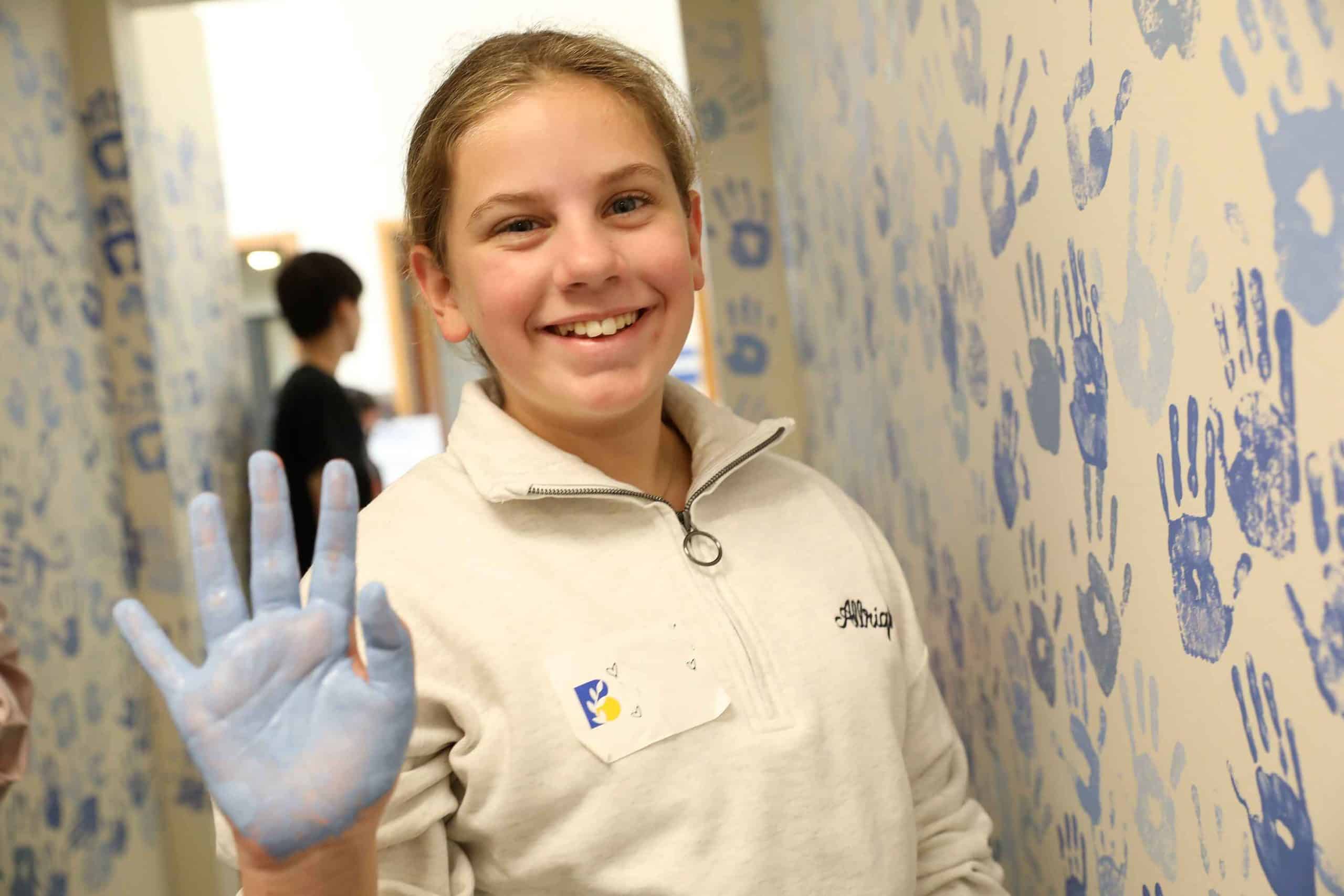 A new student adds her handprint in blue paint to the community wall