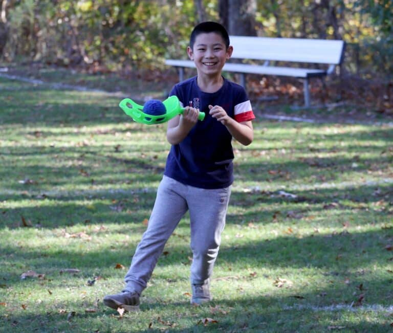 A smiling student on an athletics field holding a scoop racket