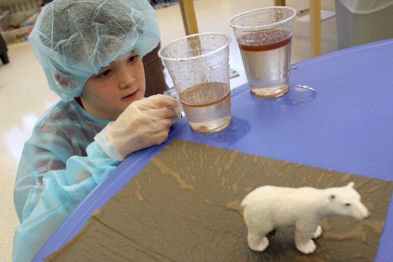 A student wearing a lab coat, hair net, and gloves conducts an experiment