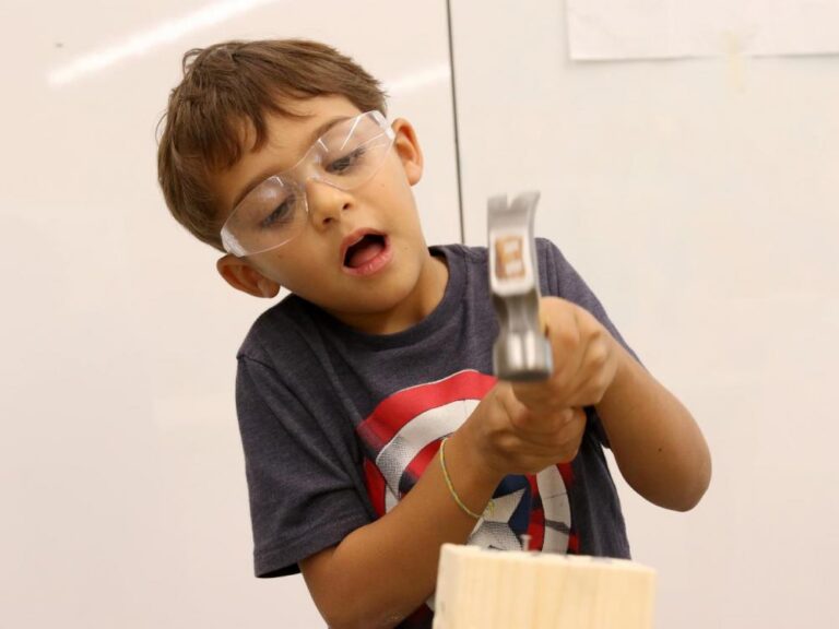 A boy uses a hammer on his project in woodworking class