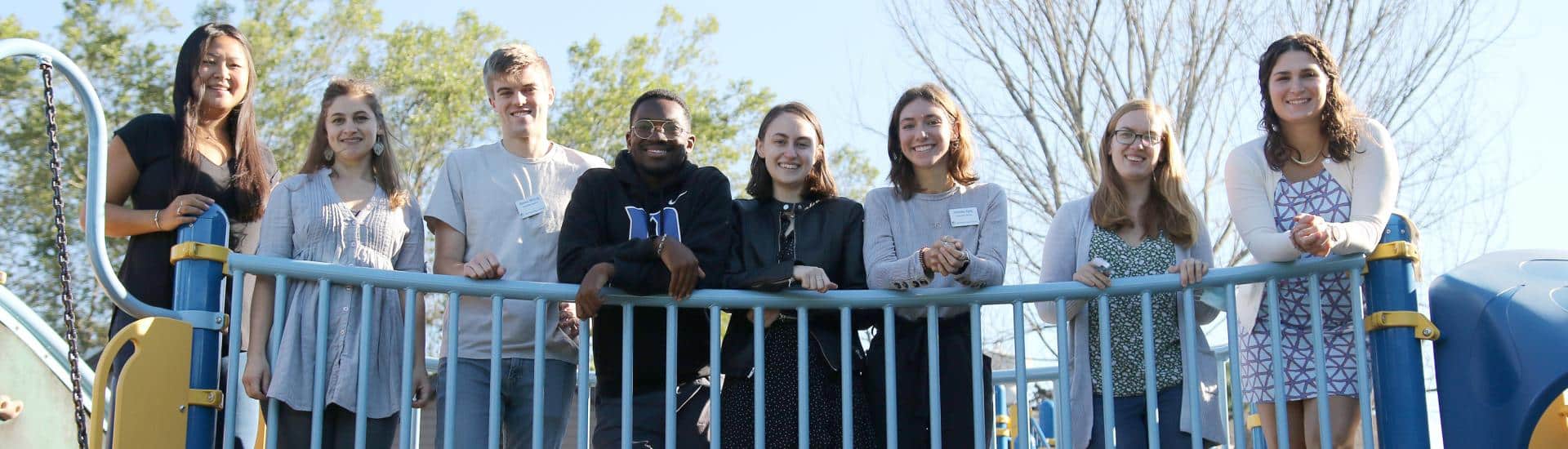 Eight people who are associate teachers stand on the bridge of the playground equipment