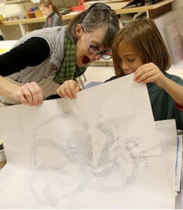 Art teacher joyfully looks at student's print in the art studio