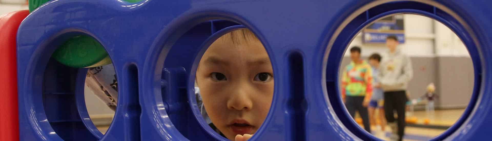 A child peeks through a structure to look at the camera