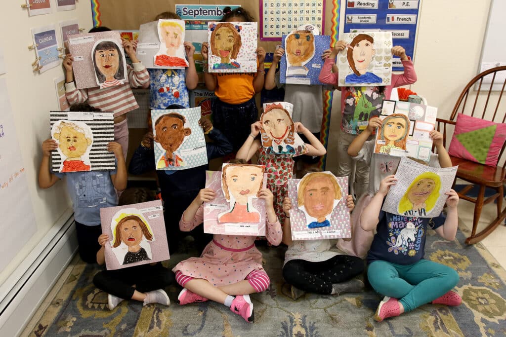 First graders hold up their self-portraits