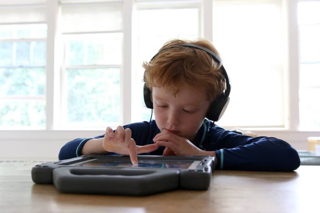 A camper wears headphones and works on an iPad at Summer Spark academic camp