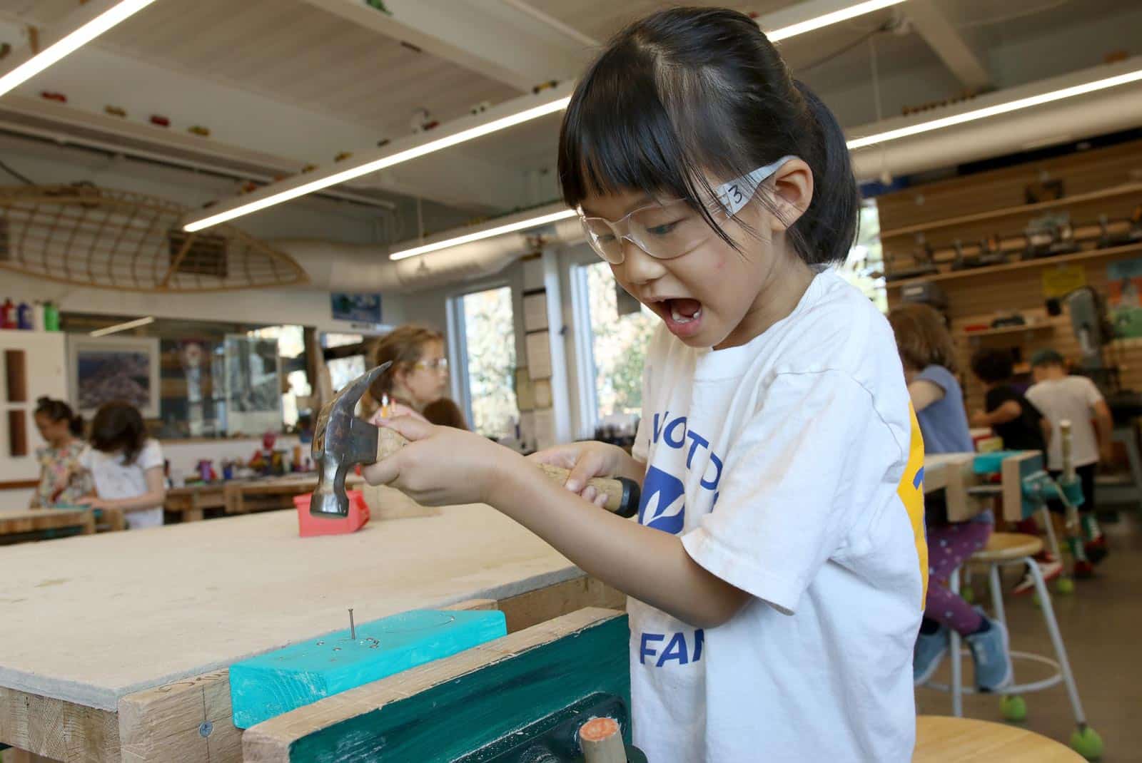 A girl hammers her project in the woodworking studio