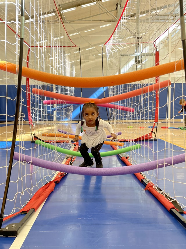 A young student navigates nets and noodles in a PE obstacle course