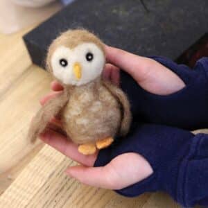 A needle felted owl held in a student's hands