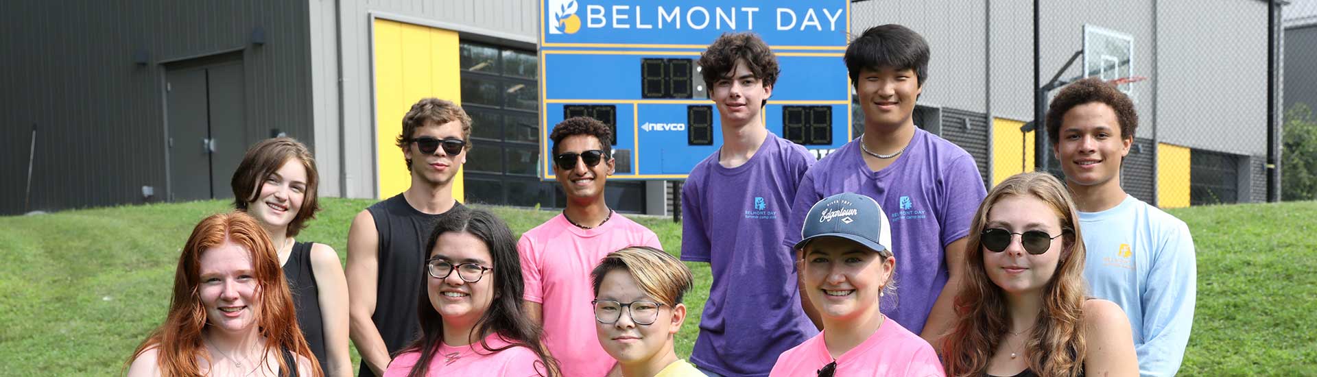 Eleven alumni summer camp counselors in front of the BDS scoreboard