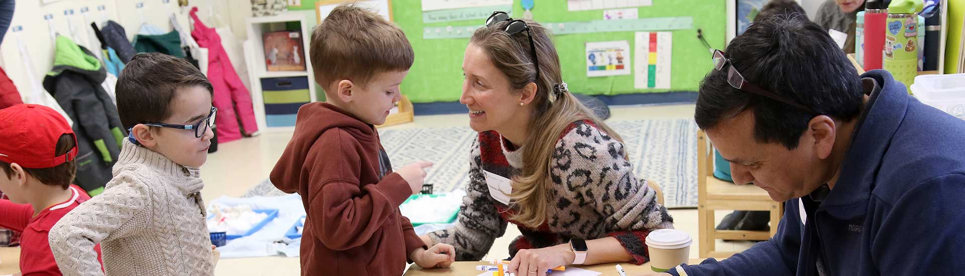 A parent grins while engaging with her child on parent sharing day