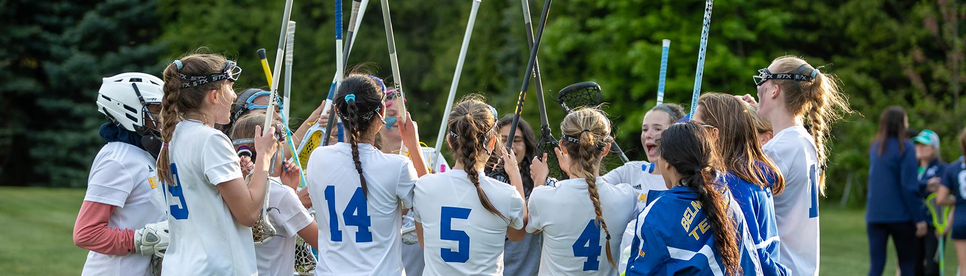 The field hockey team huddle with sticks up