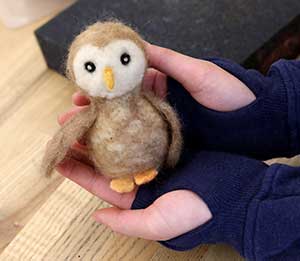 A needle felted owl in the hands of a student