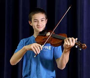 A student wearing a blue t-shirt holds his violin