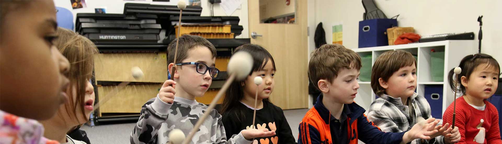 Seven pre-k students are sitting and drumming in music class