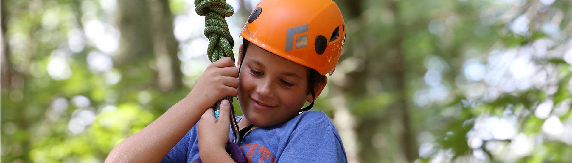 A camper wearing an orange helmet glides in the treetops at a ropes course