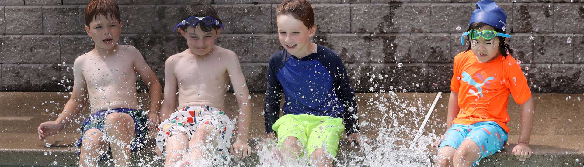 Four campers sit poolside splashing