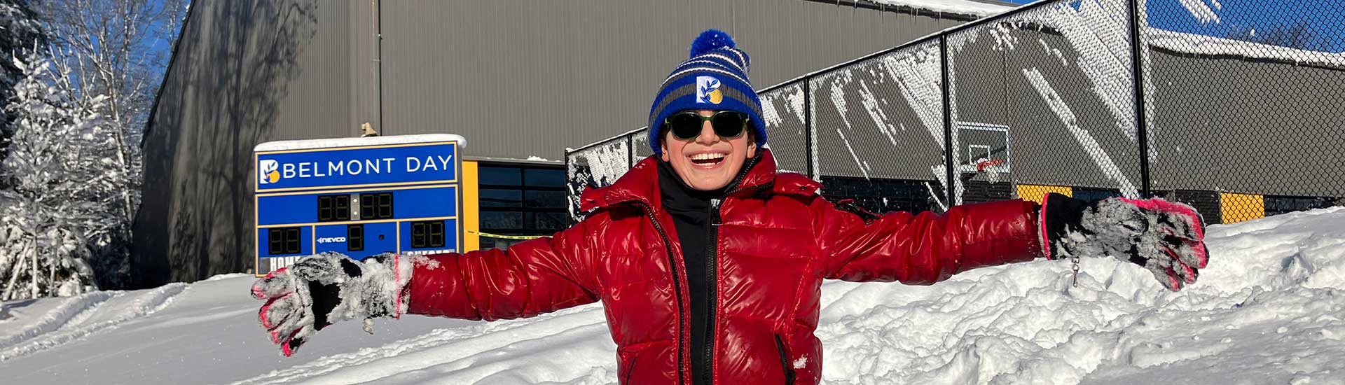 A student with arms outstretched on a snowy day in from of the campus score board